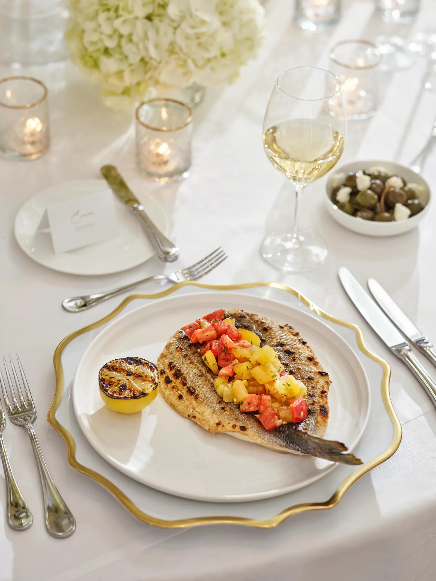 Grilled fish with citrus salsa and charred lemon on gold-rim charger.