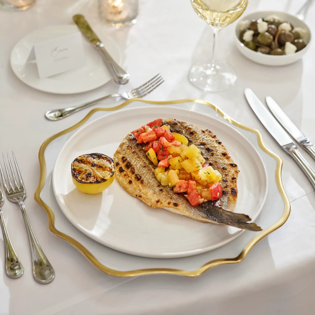 Grilled fish with citrus salsa and charred lemon on gold-rim charger.