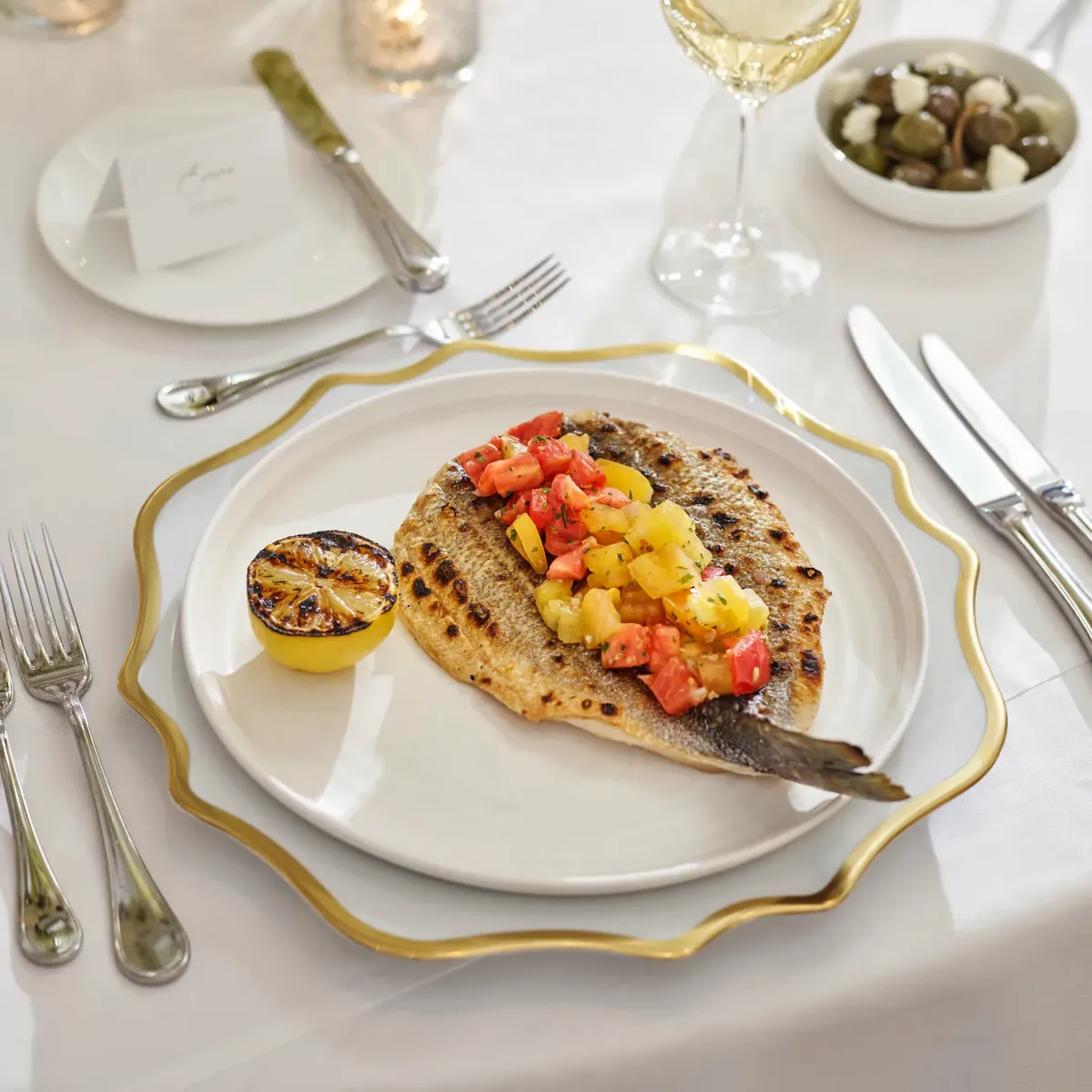 Grilled fish with citrus salsa and charred lemon on gold-rim charger.