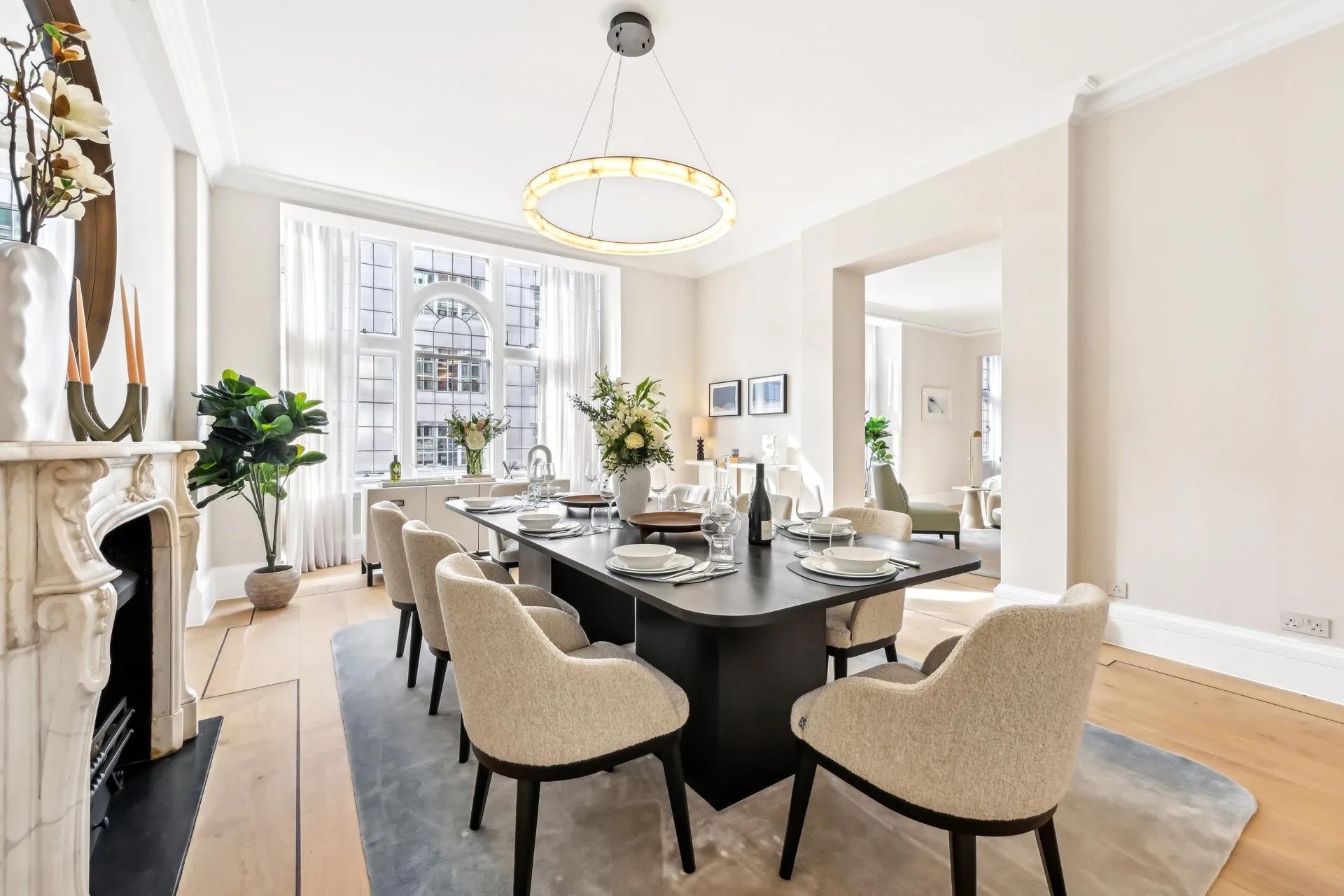 Airy dining room with a long dark table, cream chairs, chandelier, and large arched window.