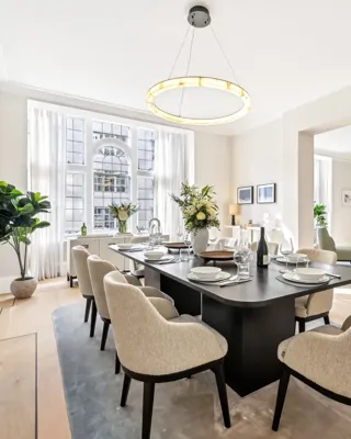 Airy dining room with a long dark table, cream chairs, chandelier, and large arched window.