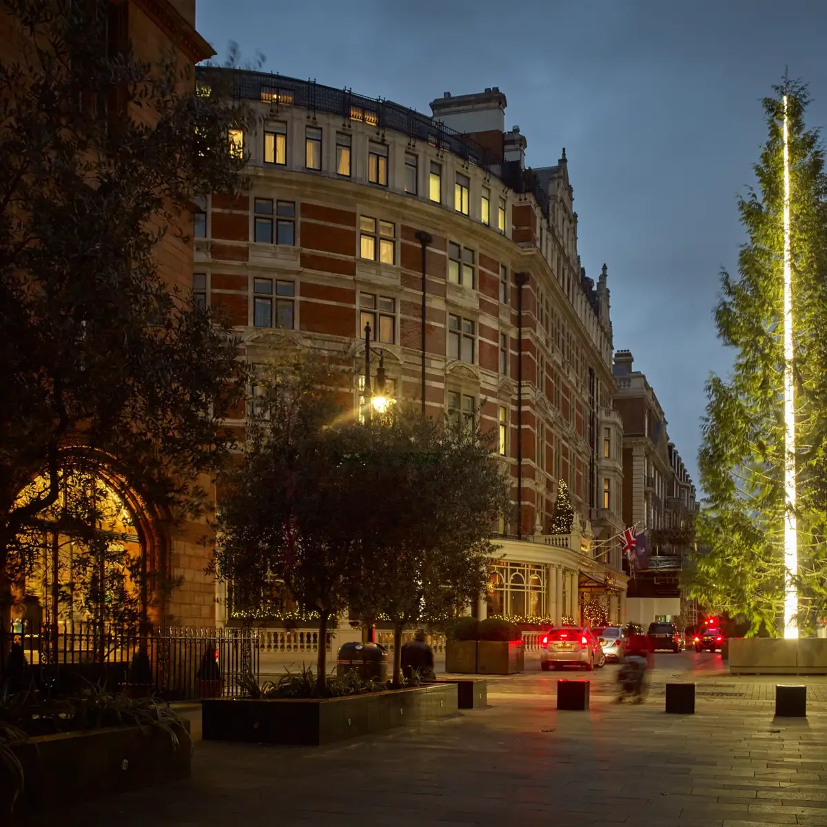 Large illuminated Christmas tree outside grand London hotel at dusk with cars passing.