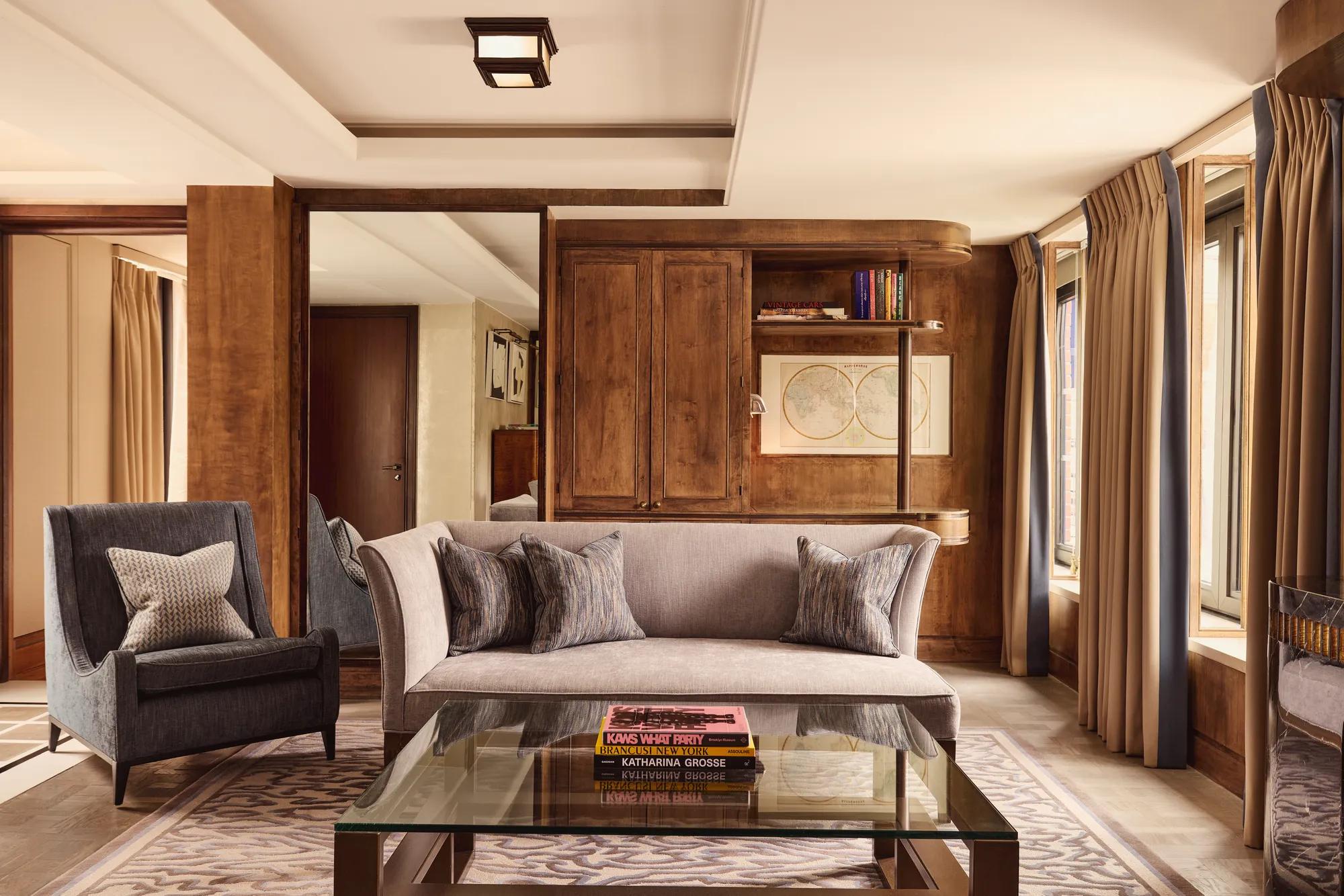 Elegant suite living room with grey sofa, armchair, wood panelling and large windows.