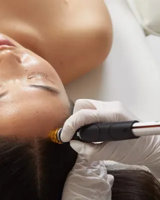 Woman receiving scalp treatment with handheld device, eyes closed, lying on treatment bed