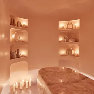 Serene spa room featuring a polished stone treatment table, softly glowing candles, and sculptural decor arranged in recessed shelves.