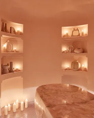 Serene spa room featuring a polished stone treatment table, softly glowing candles, and sculptural decor arranged in recessed shelves.