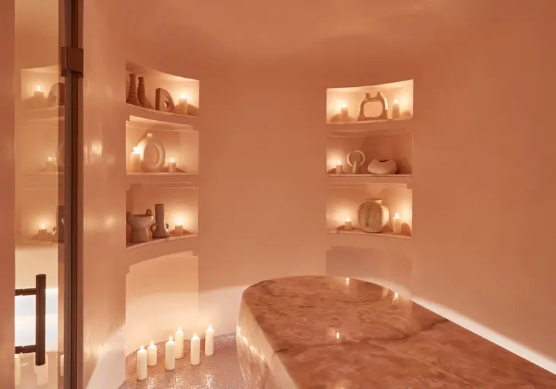Serene spa room featuring a polished stone treatment table, softly glowing candles, and sculptural decor arranged in recessed shelves.