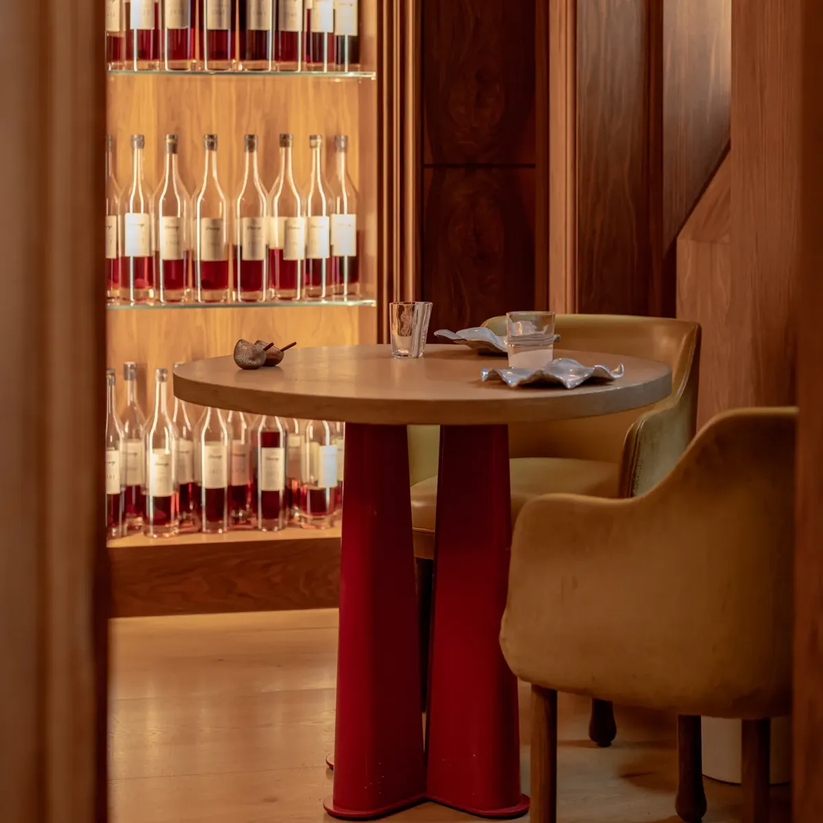 Intimate dining table with chairs set before a backlit display of wine bottles in a wood-paneled interior