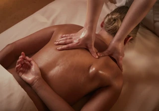 Person receiving an oil back massage on a spa bed, therapist pressing on shoulders.