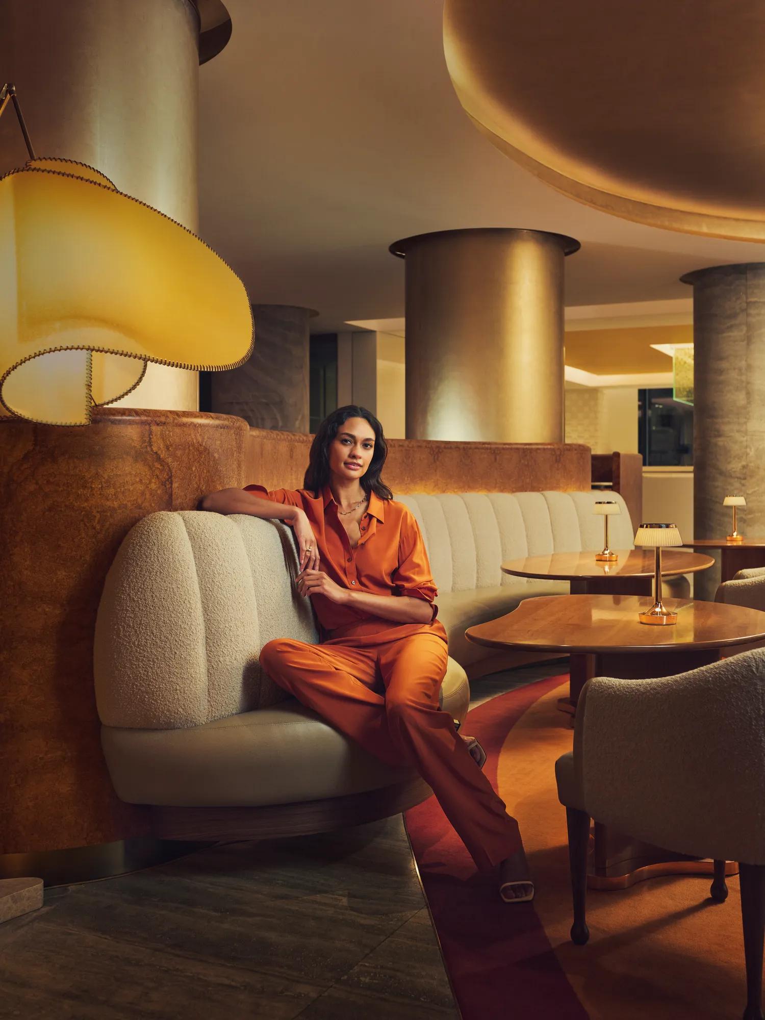 People seated in a curved banquette within a warmly lit, contemporary lounge with bronze columns and wood tables.