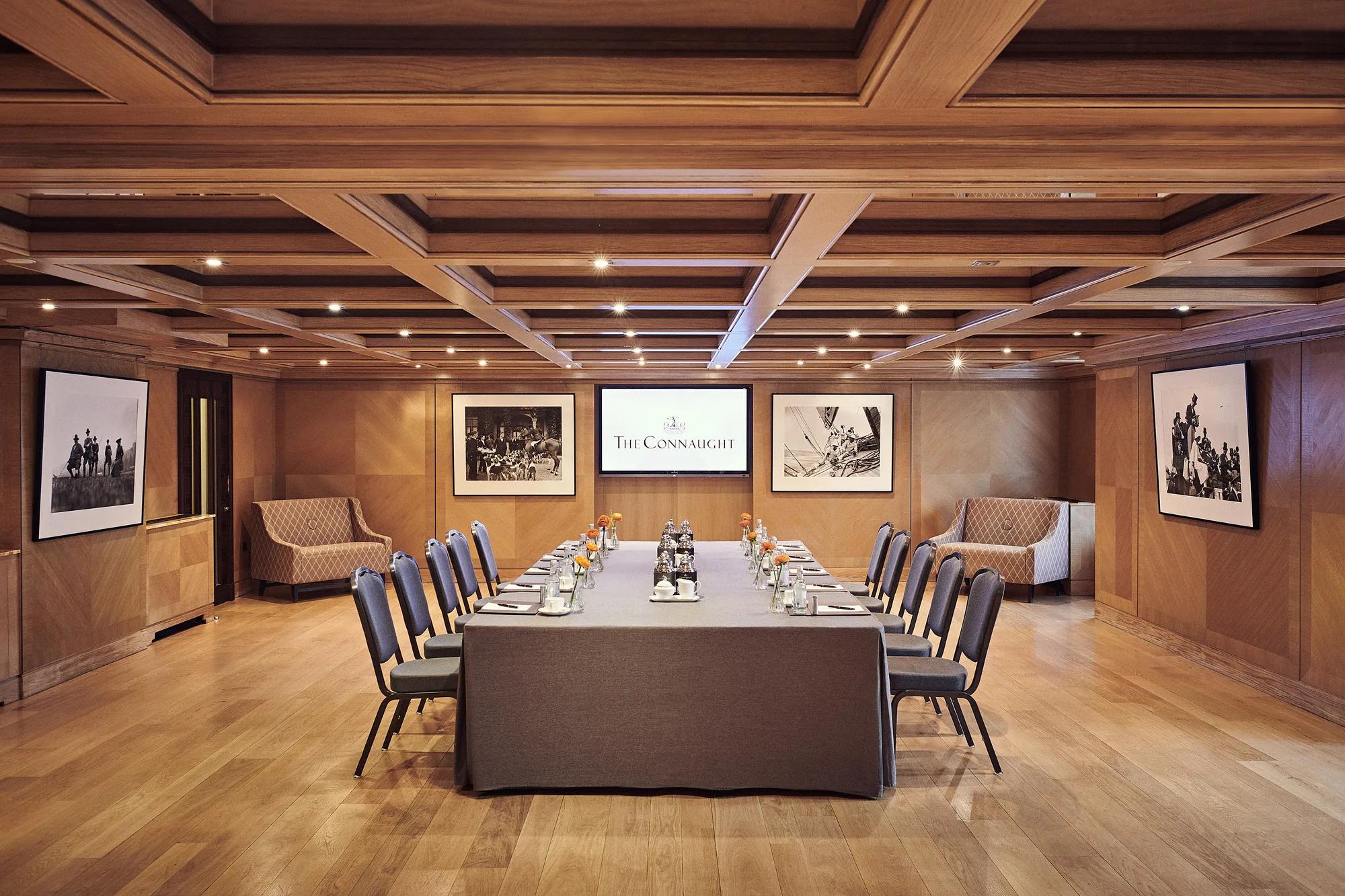 Boardroom set-up at The Connaught with a long table, grey chairs, wood-panelled walls and framed black-and-white photographs.