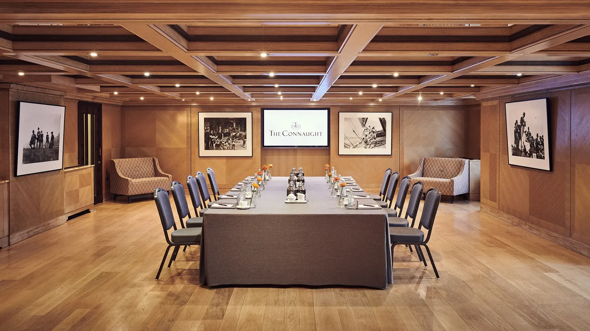 Boardroom set-up at The Connaught with a long table, grey chairs, wood-panelled walls and framed black-and-white photographs.