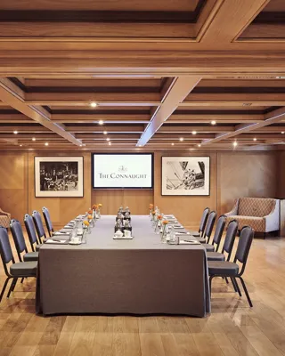 Boardroom set-up at The Connaught with a long table, grey chairs, wood-panelled walls and framed black-and-white photographs.