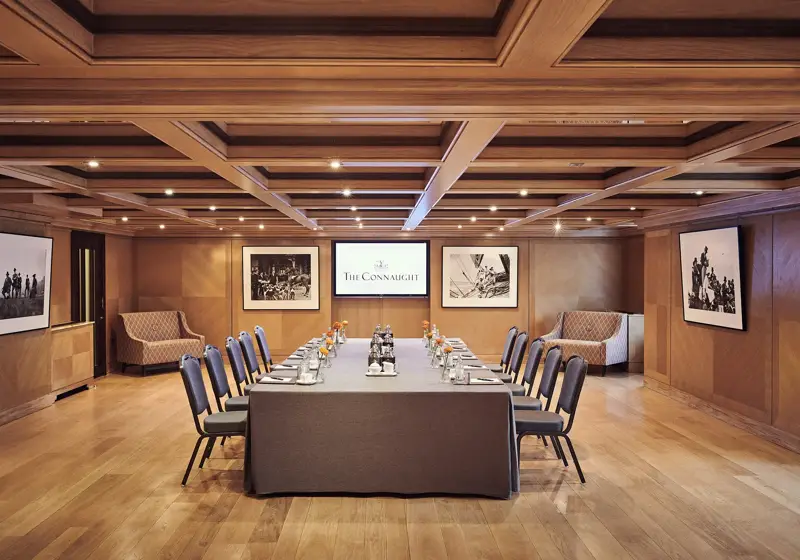 Boardroom set-up at The Connaught with a long table, grey chairs, wood-panelled walls and framed black-and-white photographs.