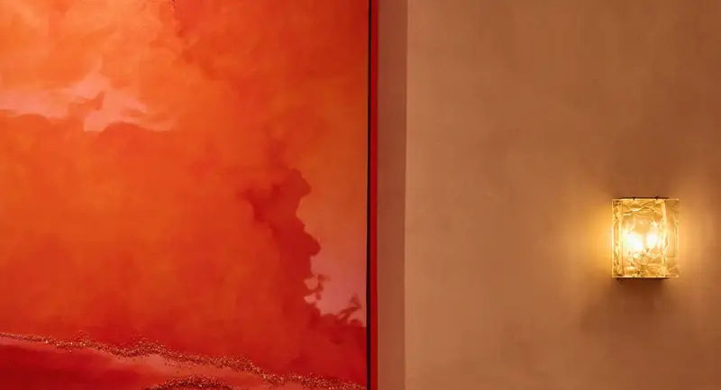 Softly lit lounge seating with curved tan banquette, marble tables, small lamps, and a large red abstract painting above.