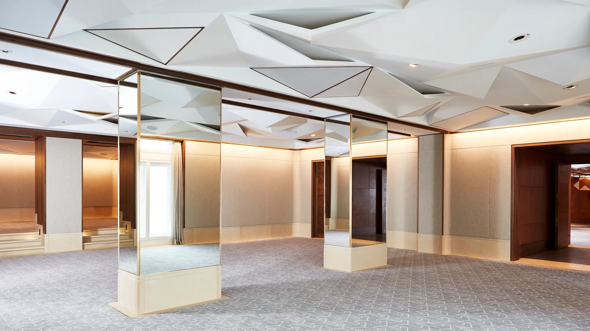 Spacious Belgravia Room with mirrored pillars, geometric ceiling panels, and light grey patterned carpet.