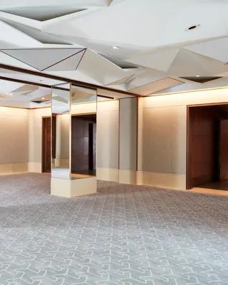 Spacious Belgravia Room with mirrored pillars, geometric ceiling panels, and light grey patterned carpet.