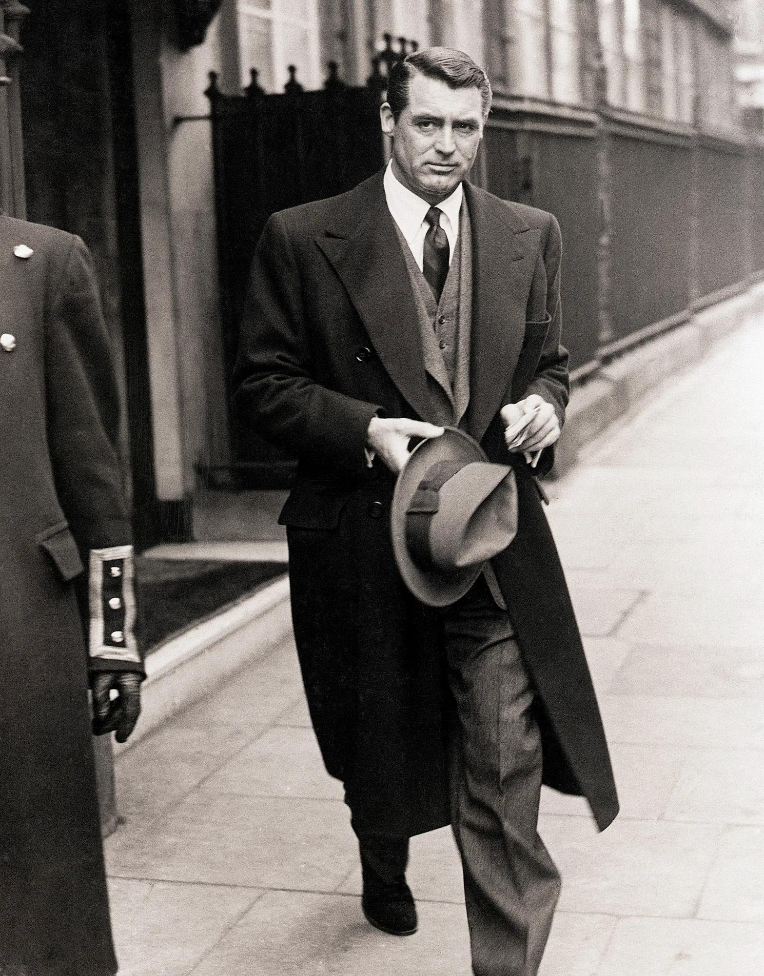 A black and white photo of a man walking in a suit