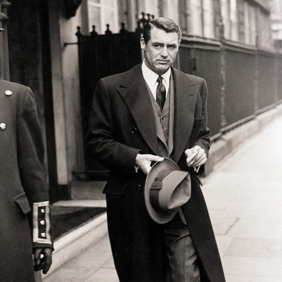 A black and white photo of a man walking in a suit