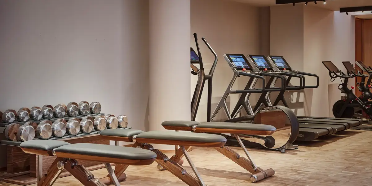 Modern fitness studio at The Maybourne Riviera featuring wooden exercise benches, polished dumbbells, treadmills, and stationary bikes on a parquet floor.