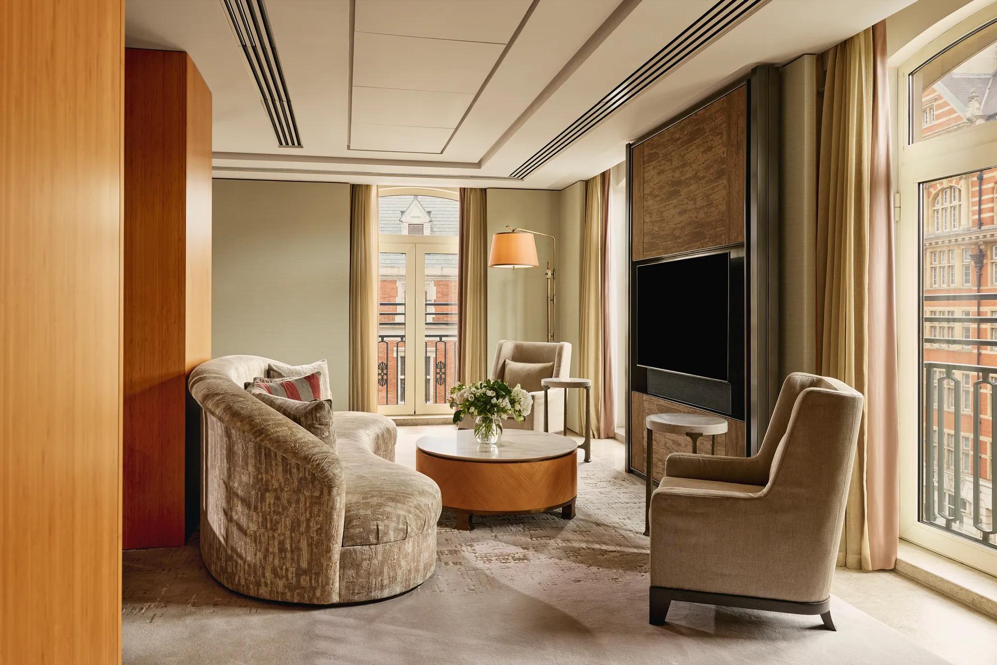 Opus Suite living area with curved sofa, armchairs, round table, and large TV by French windows