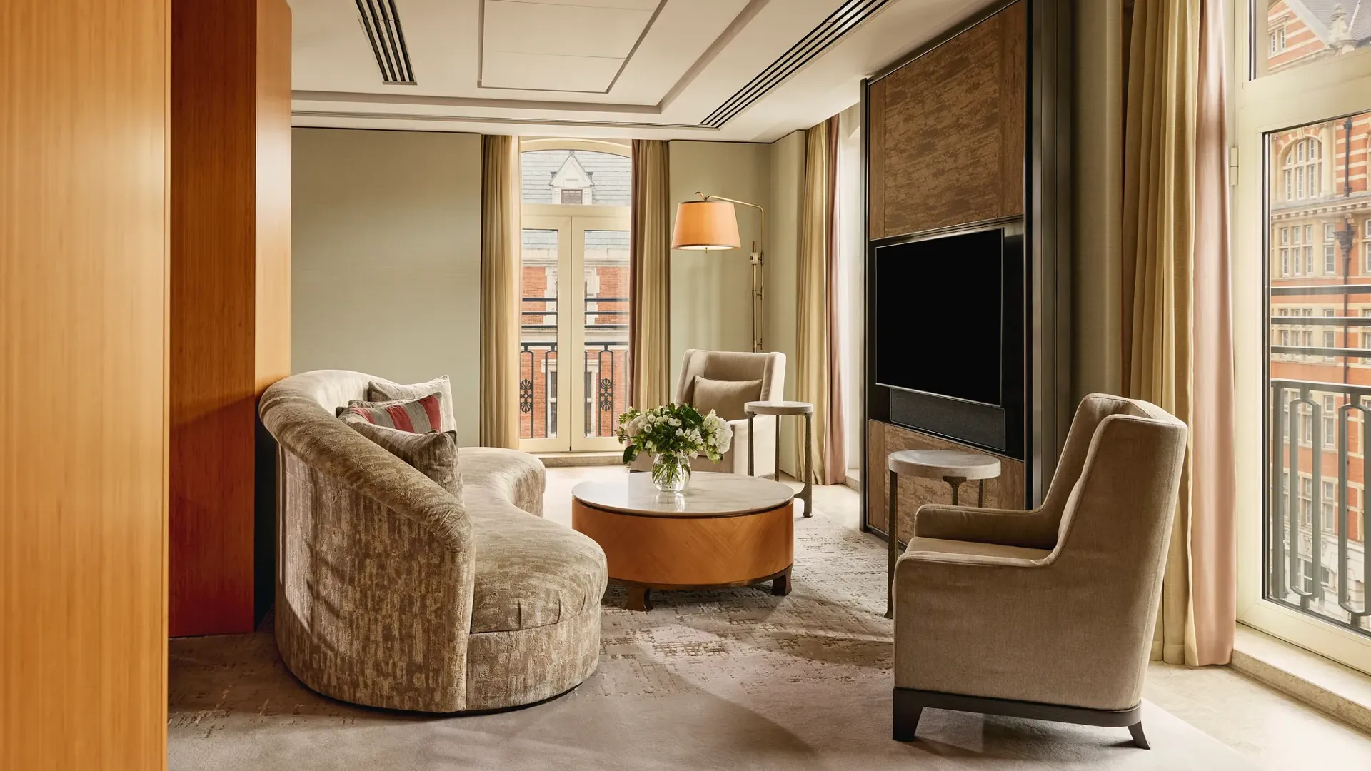 Opus Suite living area with curved sofa, armchairs, round table, and large TV by French windows