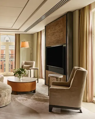 Opus Suite living area with curved sofa, armchairs, round table, and large TV by French windows