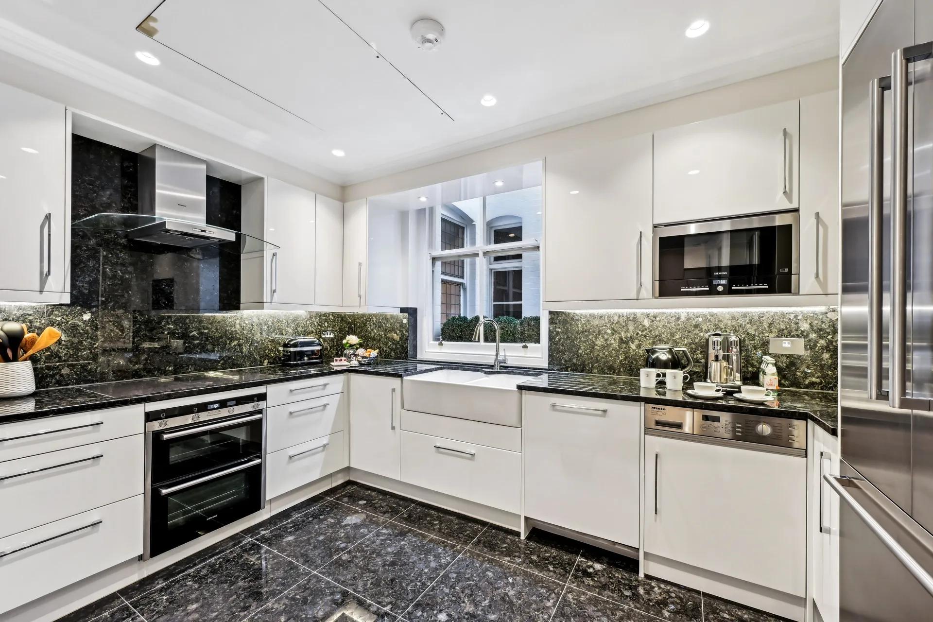 Modern white kitchen with black marble counters, built-in appliances, and a window over the sink.