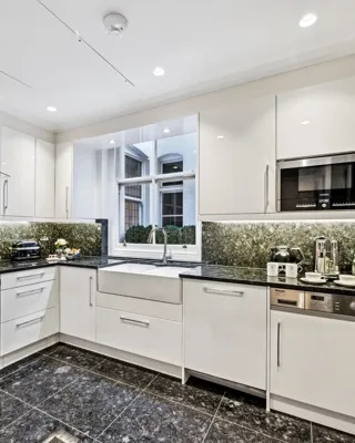 Modern white kitchen with black marble counters, built-in appliances, and a window over the sink.