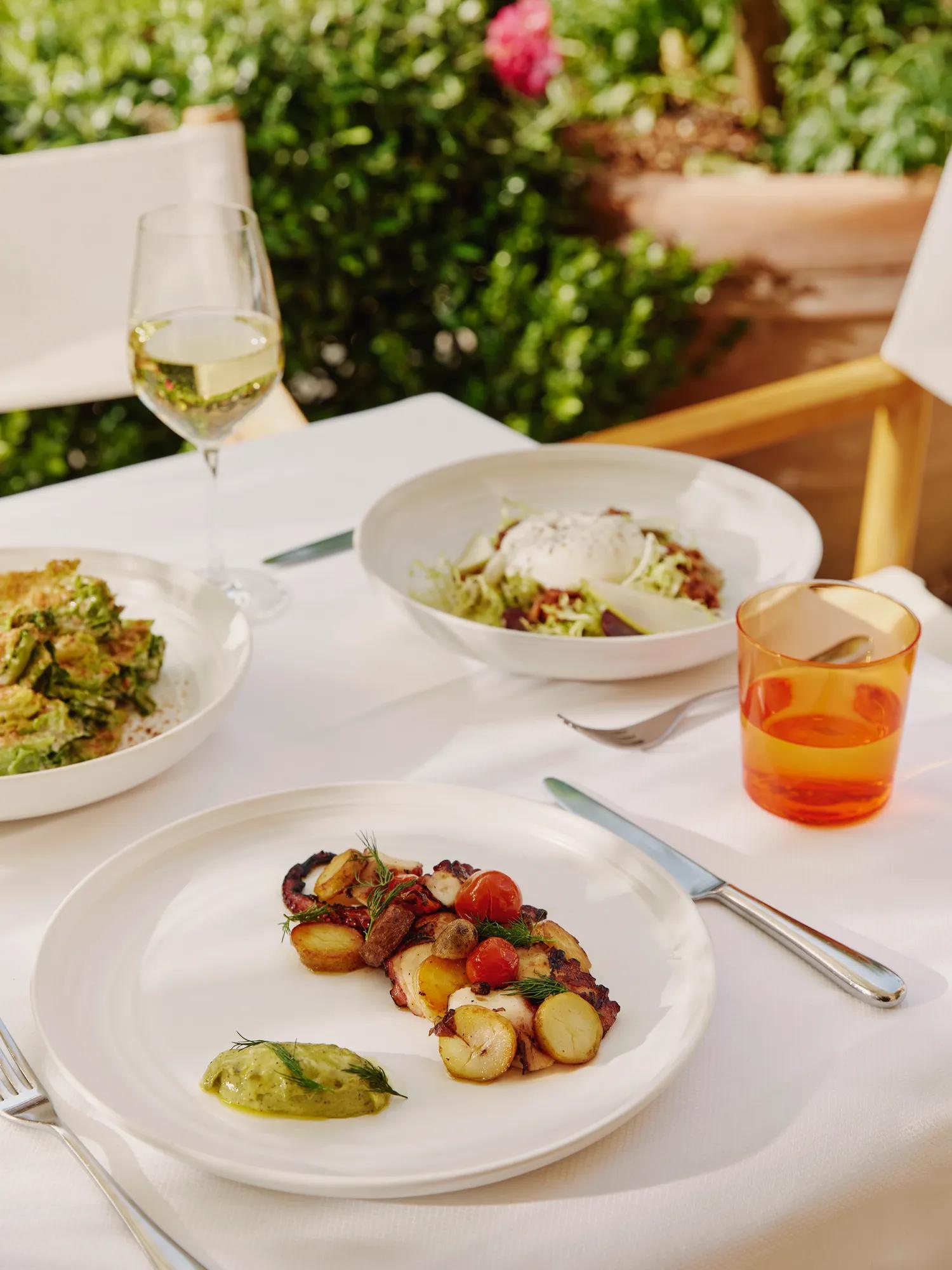 Octopus with potatoes and tomatoes on a terrace table; burrata salad and drinks in the background.