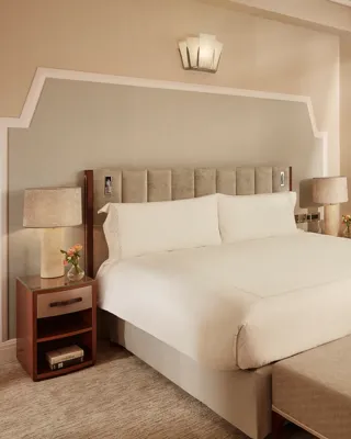 Elegant bedroom with king bed, bedside tables, chaise lounge, and large curtained window.