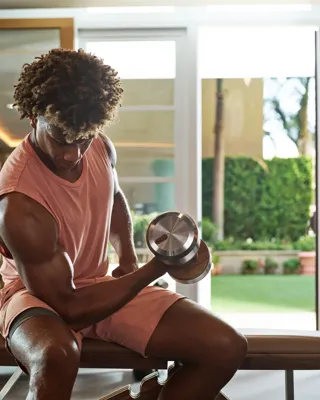 Man lifting dumbbell while seated on bench inside Maybourne Beverly Hills fitness center with mirrored walls