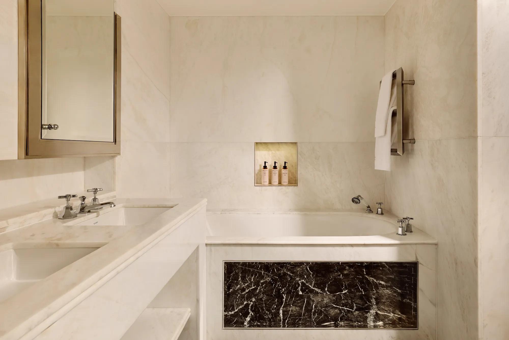 Luxurious marble bathroom with built-in bathtub, dark marble panel, double sink, and niche holding toiletries.