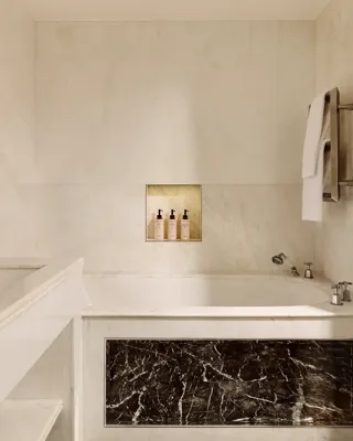 Luxurious marble bathroom with built-in bathtub, dark marble panel, double sink, and niche holding toiletries.