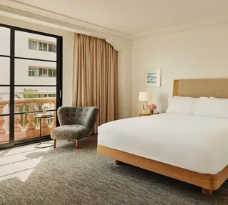 Accessible guestroom with king bed, bedside tables and lamps, lounge chair by balcony doors, and full-length curtains.