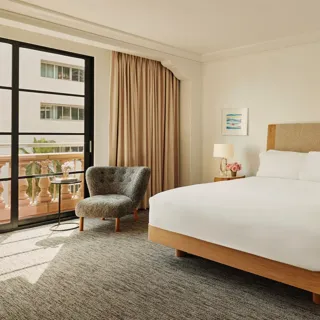 Accessible guestroom with king bed, bedside tables and lamps, lounge chair by balcony doors, and full-length curtains.