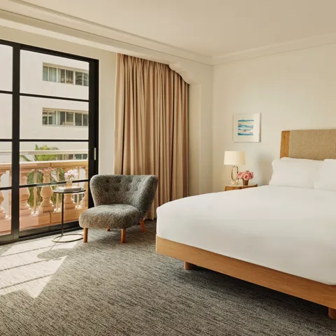 Accessible guestroom with king bed, bedside tables and lamps, lounge chair by balcony doors, and full-length curtains.