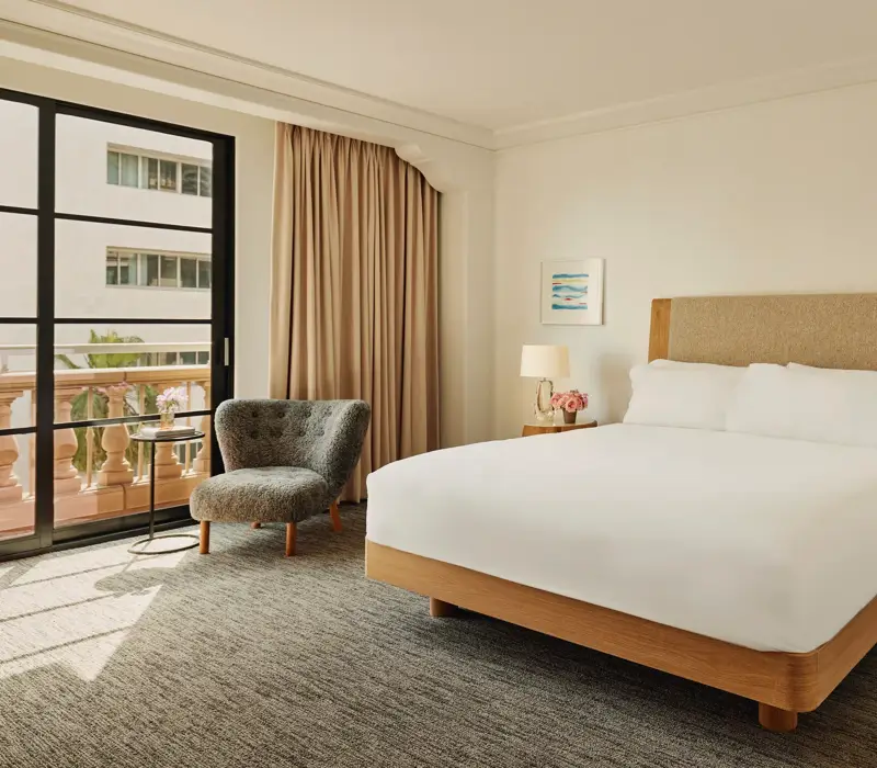 Accessible guestroom with king bed, bedside tables and lamps, lounge chair by balcony doors, and full-length curtains.