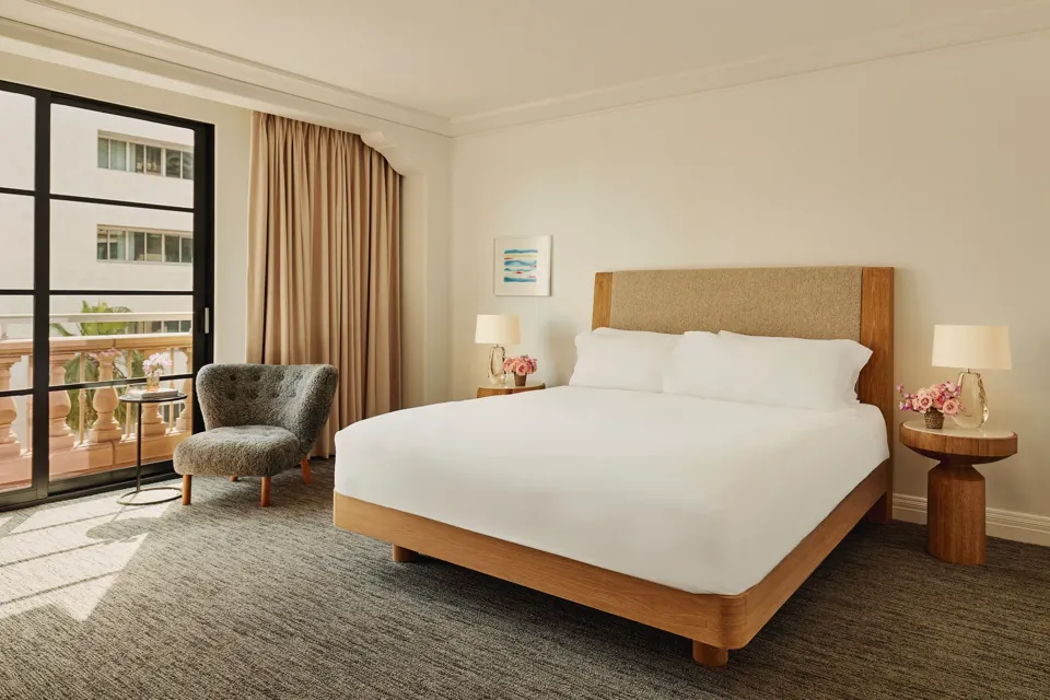 Accessible guestroom with king bed, bedside tables and lamps, lounge chair by balcony doors, and full-length curtains.