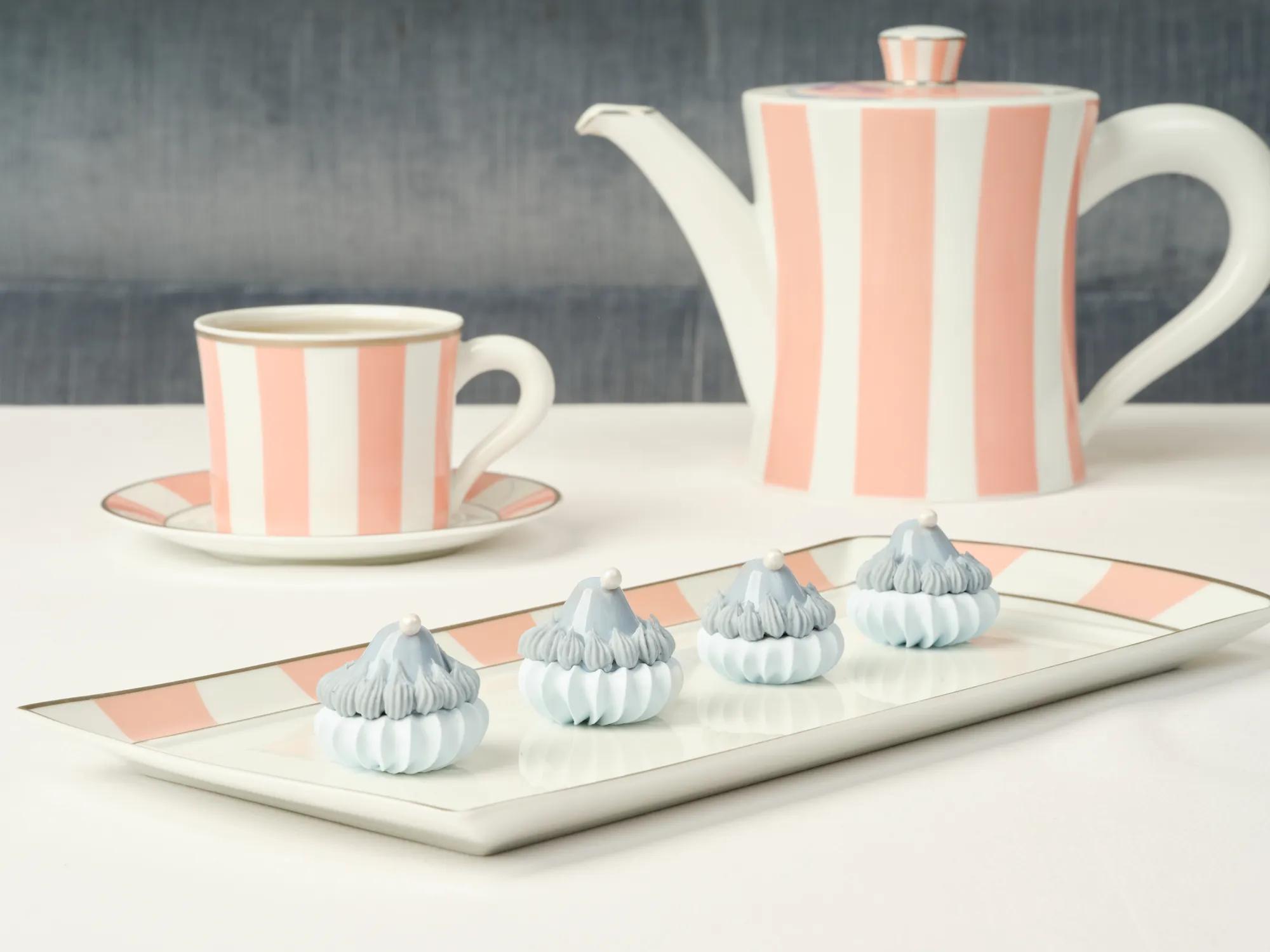Striped pink-and-white teapot set with four blue-and-white meringue treats on a tray.