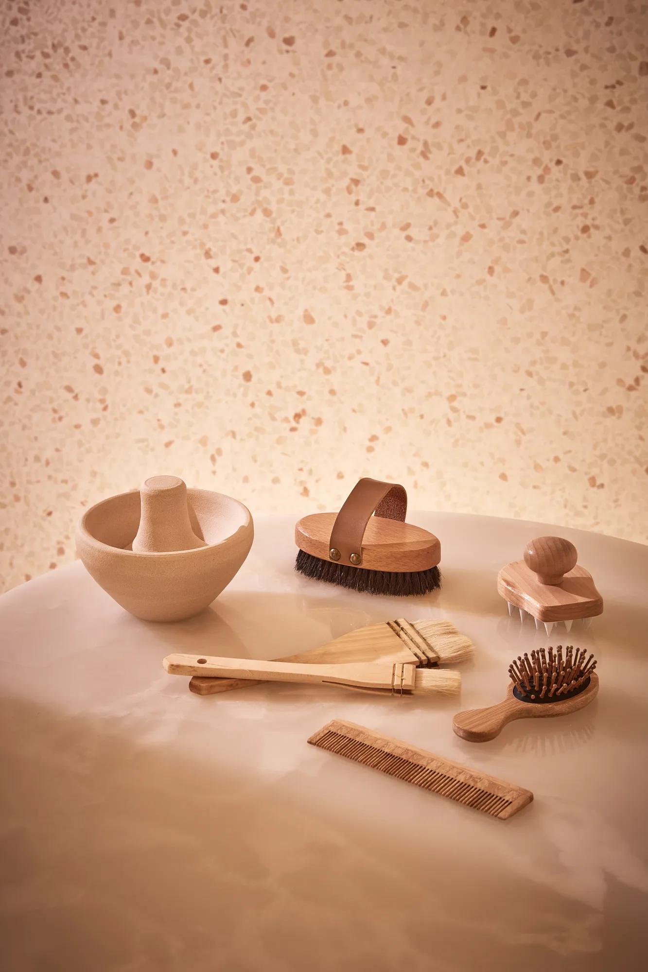 Collection of wooden spa tools, including brushes, comb, and massage accessories, displayed on a smooth stone surface