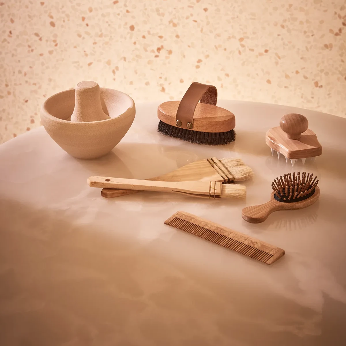 Collection of wooden spa tools, including brushes, comb, and massage accessories, displayed on a smooth stone surface