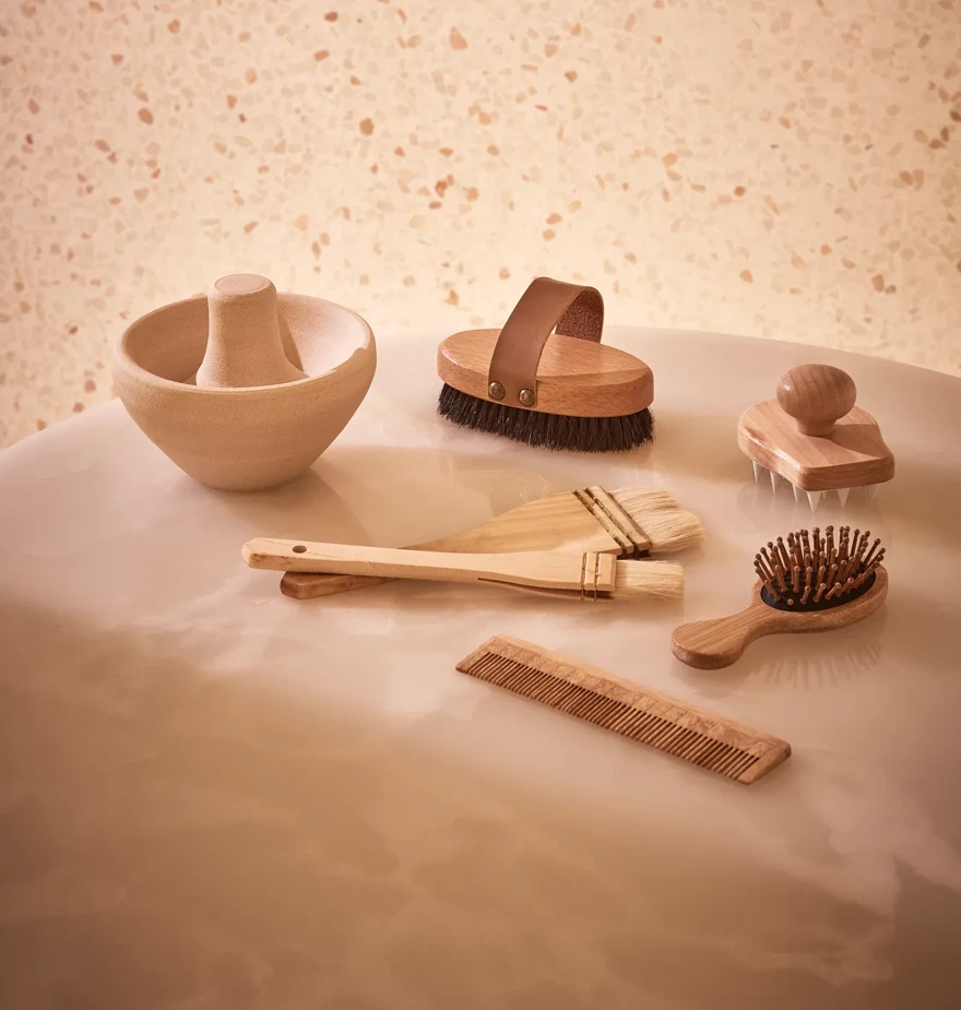 Collection of wooden spa tools, including brushes, comb, and massage accessories, displayed on a smooth stone surface