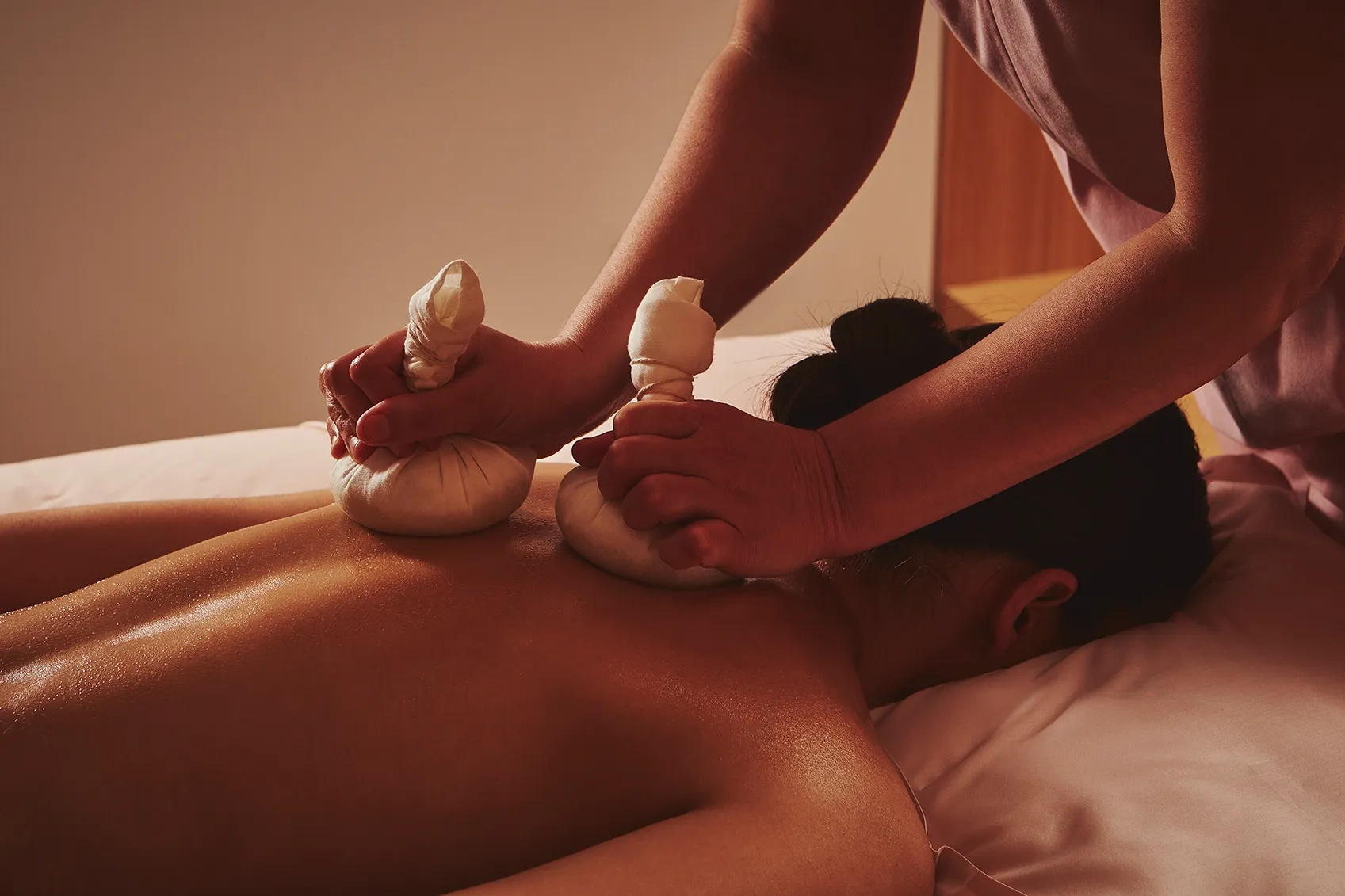 Spa therapist applying heated herbal compresses to a guest’s back during a massage treatment.
