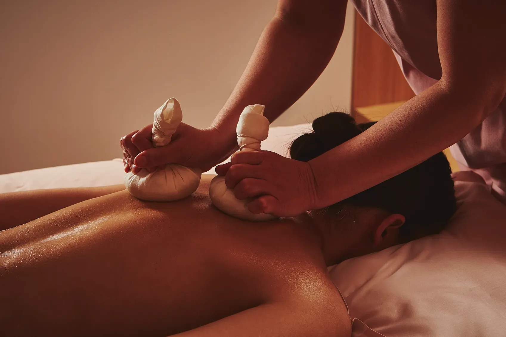 Spa therapist applying heated herbal compresses to a guest’s back during a massage treatment.