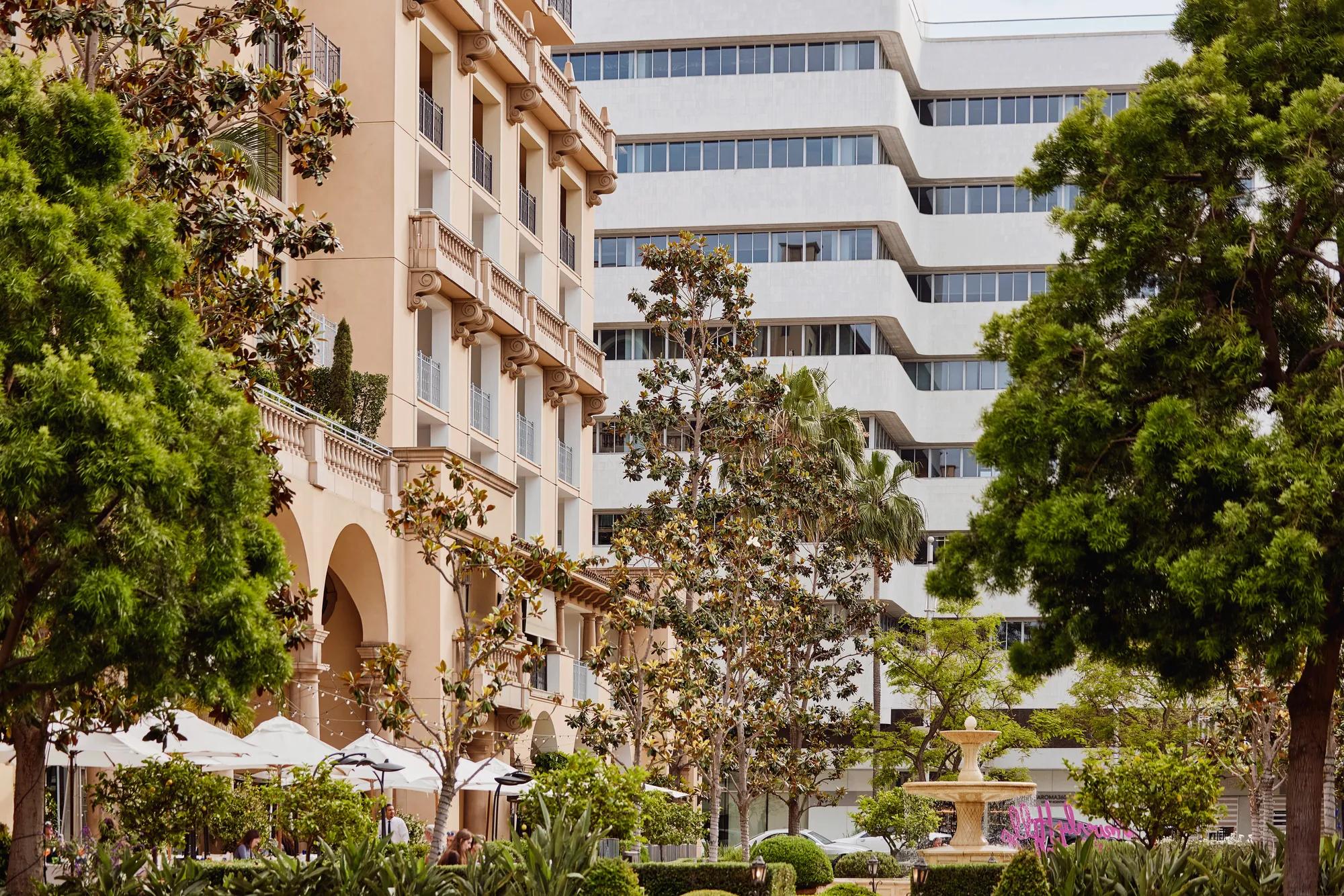 Beverly Canon Gardens with landscaped greenery, arcaded hotel façade, and a fountain in the distance.