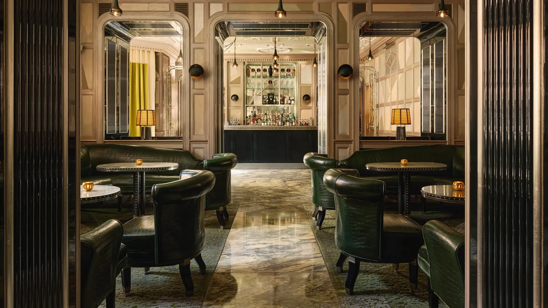 An elegant bar with dark green leather seating, marble floors, mirrored panels, and soft lighting, creating a refined, intimate ambiance.