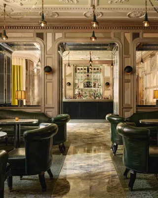 An elegant bar with dark green leather seating, marble floors, mirrored panels, and soft lighting, creating a refined, intimate ambiance.