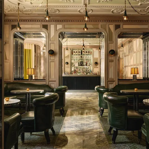 An elegant bar with dark green leather seating, marble floors, mirrored panels, and soft lighting, creating a refined, intimate ambiance.