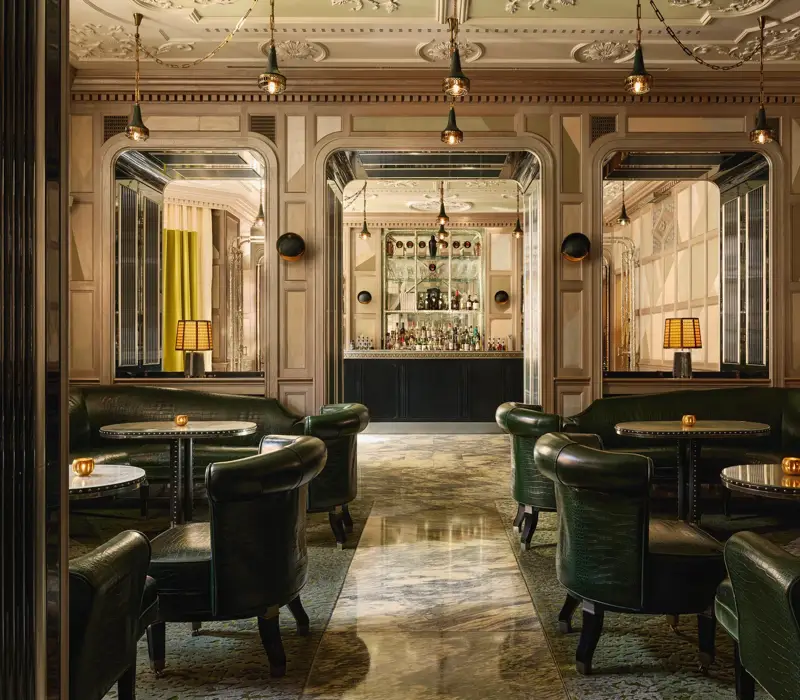 An elegant bar with dark green leather seating, marble floors, mirrored panels, and soft lighting, creating a refined, intimate ambiance.